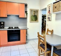 A kitchen in a 3-room apartment with orange cabinets, a dining set placed, and decorations on the walls.