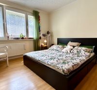 Bedroom in a 3-room apartment with a bed, wood-patterned flooring, and a white chair.