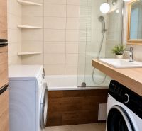 Bathroom with a bathtub, washing machines, and a sink in a 3-room apartment, tiles and wooden decor.