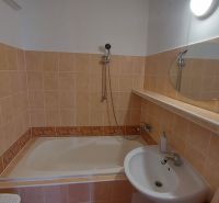 Bathroom in a 2-room apartment with a bathtub, sink, and simple mirror.