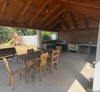 A gazebo at a family house in Iža with wooden furniture and a children's playground in the garden.