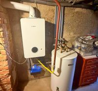 Boiler and water heater in the utility room of a family house with a brick wall.