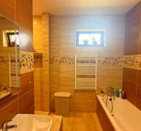 A bathroom in a family house with ceramic tiles and a bathtub.