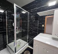 A bathroom in a family house with black tiles, a shower enclosure, and a white sink.