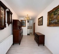 A hallway in a family house with antique furniture, paintings, and a chandelier, with a wooden decor floor.
