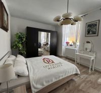 A bedroom in a family house with a wooden decor floor, a bed, and a mirrored wardrobe.