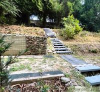 Stone steps leading through the forest to a cabin in Bratislava IV are surrounded by dense trees.