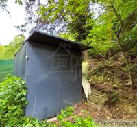 A small metal structure surrounded by greenery next to a cottage in Bratislava IV.