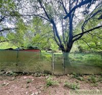 A cottage in Bratislava IV with a fence surrounded by lush greenery and trees.