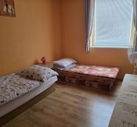 A room with two beds, a wooden decor floor, orange walls, curtains, a window.