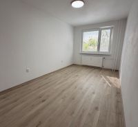 A room with a wooden decor floor in a 2-room apartment, white walls, and a window.