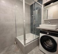 Shower corner and washing machine in the bathroom of a 2-room apartment with ceramic tiles.