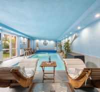 A blue interior of a family house with a pool, loungers, and plants.