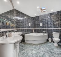 A bathroom in a family house with dark tiles, a bathtub, a toilet, and sinks.