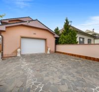 A family house in Bernolákovo with a garage door and a paved driveway amidst greenery.