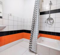 A bathroom with orange and black tiles, a shower corner, and a curtain with a geometric pattern.