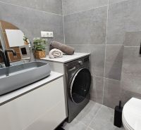 A bathroom with a washing machine and gray tiles in a 2-room apartment.