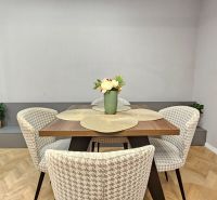 Dining area with flowers and chairs in a 2-room apartment with wood-patterned flooring.