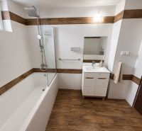 A bathroom in a family house with a bathtub and a wooden decor floor.