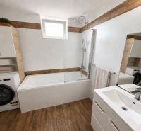 Bathroom with a bathtub, washing machine, and wooden decor flooring in a family house.