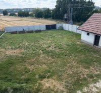 The yard of a family house on Hoštáky Street in Dojč with a green lawn and fields in the background.