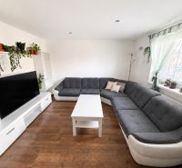Living room in a family house with a large sofa, television, and floor with wooden decor.