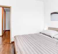 A bright bedroom with wood-patterned flooring and a large bed in a two-room apartment.