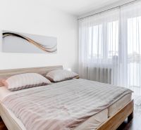A bedroom with light furniture, a wooden decor floor, and curtains in a two-room apartment.