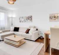 Living room in a 2-room apartment with a wooden decor floor, beige sofa, and dining table.