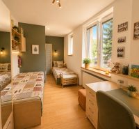 A children's room with two beds, wooden floor decor, and a large window.