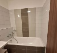 A bathroom with a bathtub and gray tiles in a 2-room apartment.