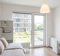 Studio apartment with a bed, shelf, desk, and a view of the balcony, floor with wood decor.