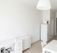 A studio apartment with wood-patterned flooring, white furniture, and a kitchen.