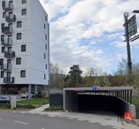 Parking on Hraničná Street in Bratislava-Ružinov in front of modern garages and an apartment building.
