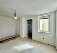 A room in a family house with plastered walls and an open window, without flooring.