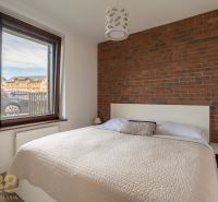A bedroom in a 2-room apartment with a brick wall and a window with a view.
