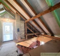 The attic of a family house with exposed wooden beams and a staircase to other areas.