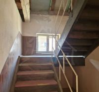 A staircase in a family house, walls with peeling plaster, wooden beams on the ceiling.