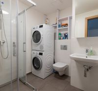Bathroom with a washing machine and dryer in a studio apartment, light tiles and a shower corner.