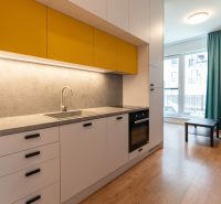A kitchen in a studio apartment with yellow cabinets and a wooden decor floor.