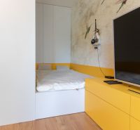 A bedroom in a studio apartment with a bed, TV, and wooden decor flooring.