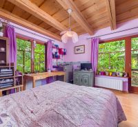 The interior of a family house with a wooden ceiling, purple curtains, and a bed.