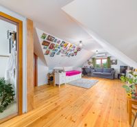 Attic room with a bed, sofa set, and wooden decor flooring in a family house.