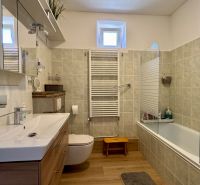 A bathroom in a family house with a bathtub, a floor with a wooden decor, and modern elements.