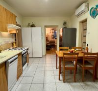 A kitchen in a family house with four chairs, appliances, and a clock on the wall.