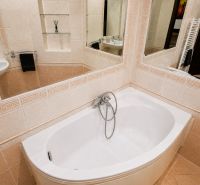 A bathroom with a rounded bathtub and a mirror in a 2-room apartment.