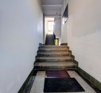 The entrance hallway of an apartment building with a stone floor and staircase.