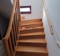 The staircase with a wooden decor leads in the Family house to a small window and a railing.