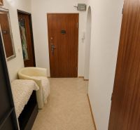 A hallway in a 4-room apartment with tiles, wooden doors, and a light chair.