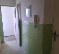A corridor with white and green walls, a door to a room, a phone on the wall.